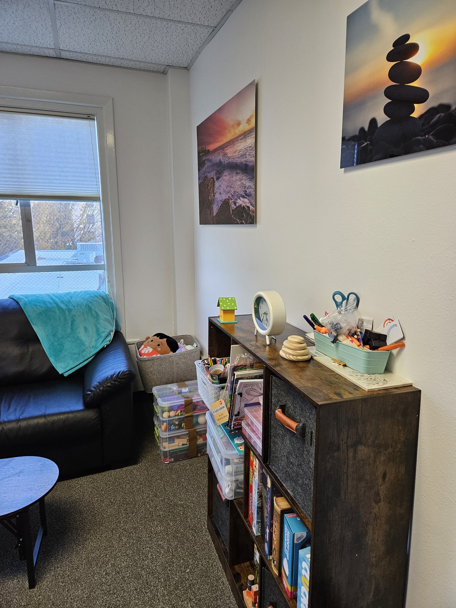 A couch with a blanket, a low table and a shelf of games beside a window